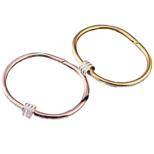 Two gold and rose gold tone hinged bangle bracelets. Each one features a slender, slightly oval band adorned with a row of small zircons  along its upper edge, making them a sophisticated accessory for various occasions.