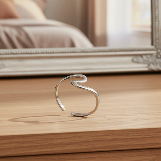 Silver open wave ring on a dresser. This ring is a versatile accessory that complement various styles, drawing attention to its unique form rather than intricate details.