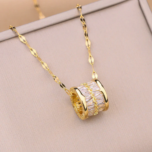 The pendant showcases a luxurious barrel design, completely adorned with sparkling baguette-cut stones, separated by a central gold-tone band.