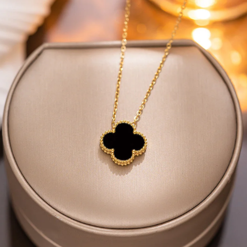 Gold necklace with a black clover pendant on a beige jewelry box. This is a close up of the back clover pendant.