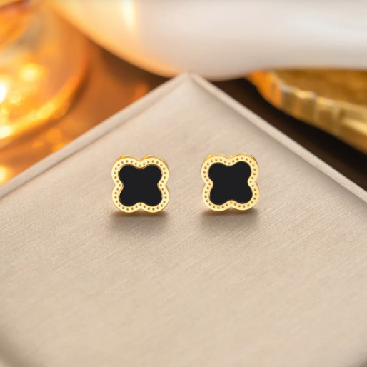 Gold plated stainless steel enamel black clover stud earrings. Each one has a prominent black inlay framed by a polished gold metal border, which is detailed with a delicate dotted texture. Their stainless steel construction gives them durability and low maintenance.