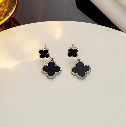 This pair of earrings features a contrasting design with black clovers in a silver tone border. This metal is 18K white gold over stainless steel.