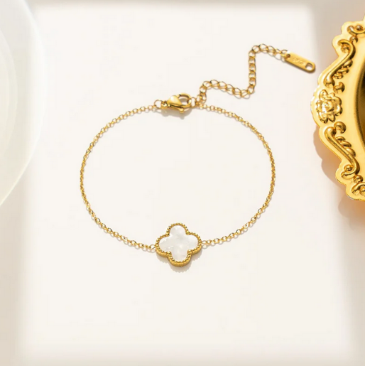 Gold bracelet with a white clover-shaped charm, and a extender.
