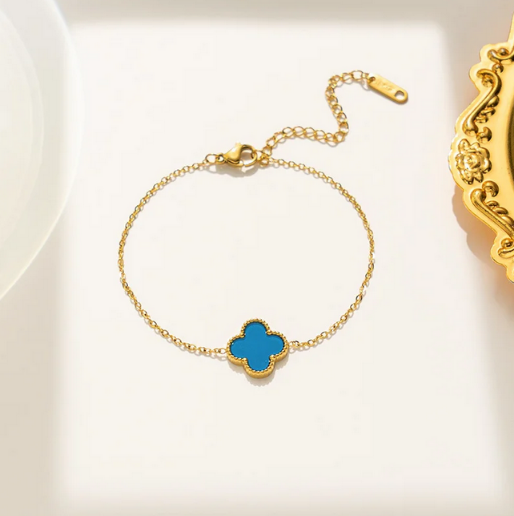 Gold bracelet with a blue clover-shaped charm. The delicate, thin gold-toned link chain, giving a dainty and elegant appearance. 