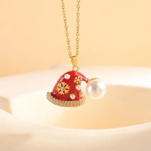 Charming necklace featuring a meticulously designed pendant shaped like a classic Santa hat. The hat is adorned with vibrant red enamel, detailed gold snowflake patterns, sparkling clear cubic zirconia stones, and delicate simulated pearls. The entire pendant is suspended from a fine gold toned link chain.