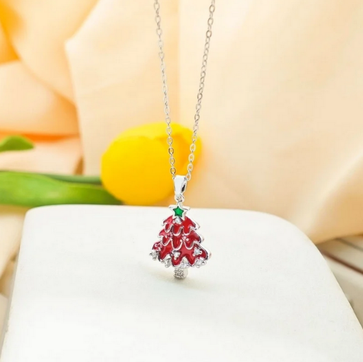 Festive necklace featuring a detailed Christmas three pendant, showcasing a bright red enamel design, layered to resemble the branches of a Christmas tree. It hangs from a delicate silver-toned chain,
