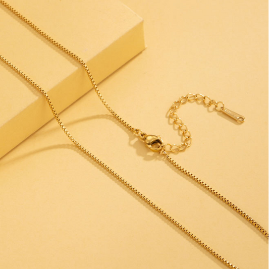 Gold box necklace on a yellow background