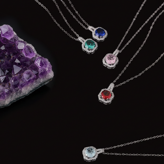 Silver necklaces with gemstones next to an amethyst crystal on a black background