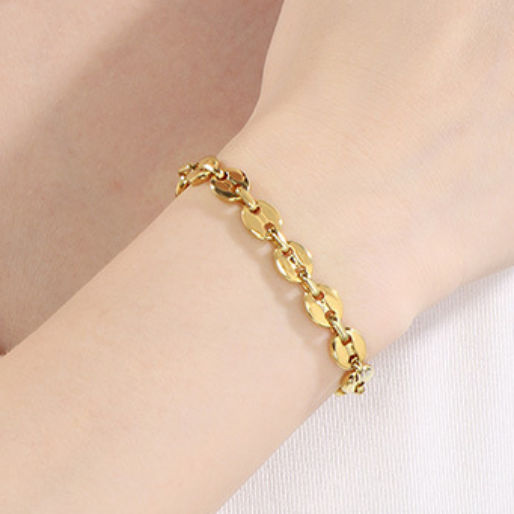 Gold mariner chain bracelet on a wrist with a plain background