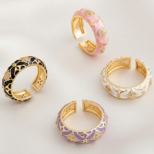 Four gold rings with multiple color enamel and beautiful accents on a silky white surface