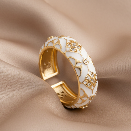Gold and white enamel open ring with floral designs on a brown textured surface
