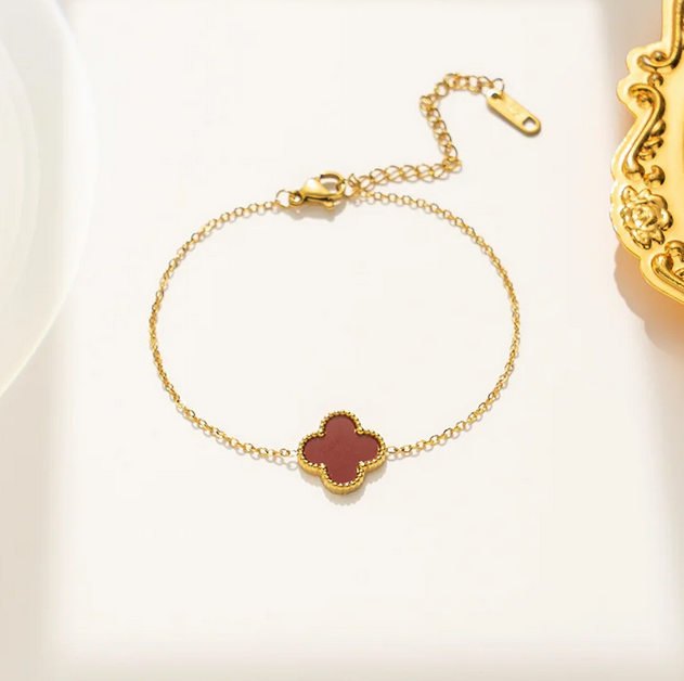 Gold bracelet with a red clover-shaped charm, and a extender that makes their size adjustable.
