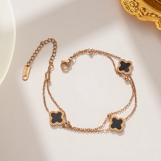 Rose gold double chain bracelet with black clover-shaped charms, and small gold beads. The rose gold finish is bright and uniform, creating a luxurious contrast with the deep black of the clover inlay.