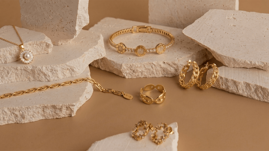 Gold jewelry including bracelets, rings, and necklaces on a textured beige surface.