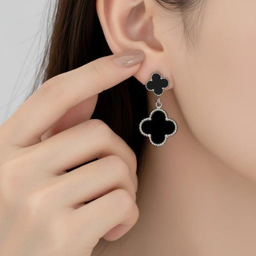Black clover-shaped dangle earrings being worn, showing the beauty and elegance of the design.